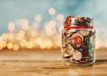 Donation money jar filled with coins in front of holiday lights
