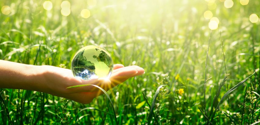 Earth crystal glass globe in human hand on fresh juicy grass background. Saving environment and clean green planet concept. Card for World Earth Day.