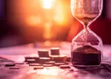 Sand running through the shape of hourglass on table with banknotes and coins of international currency. Time investment and retirement saving. Urgency countdown timer for business deadline concept