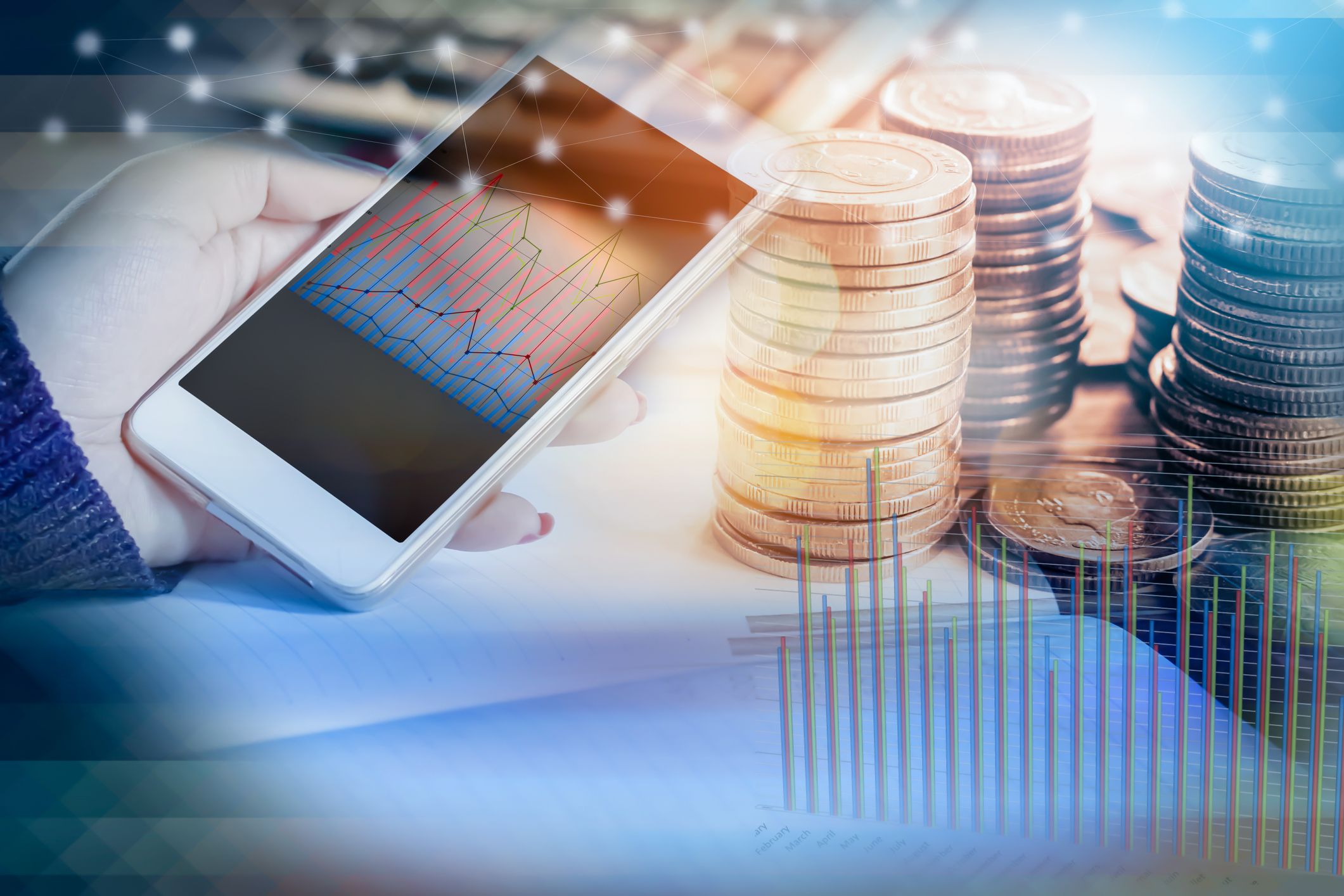 double exposure of hand holding smart phone with financial graph, stack of coins