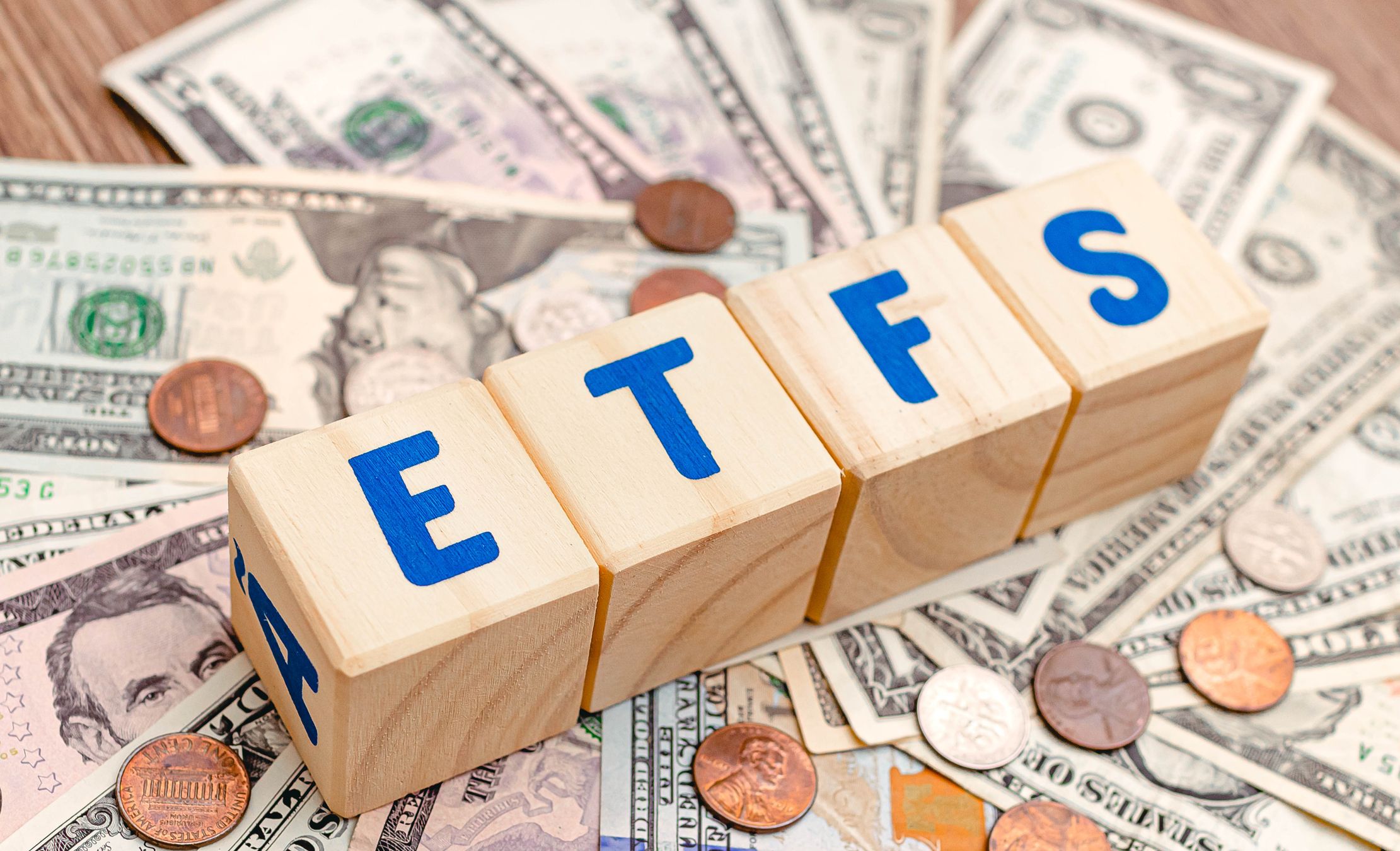 Wooden cubes with blue letters forming the word ETFS (Exchange Traded Funds) on dollar bills on a table. Investment concept photo.