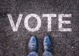 Legs and shoes on asphalt with the word “vote”