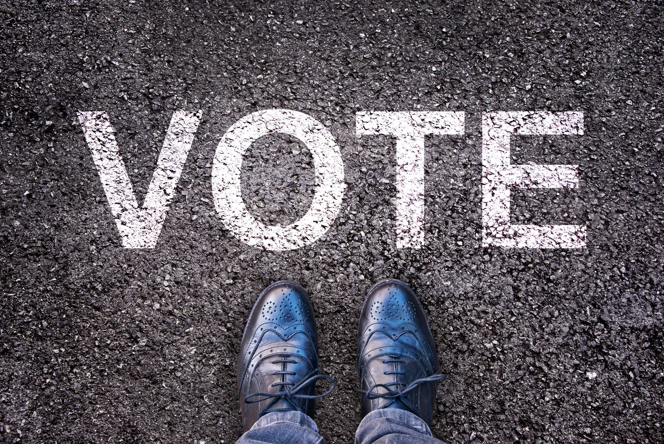 Legs and shoes on asphalt with the word “vote”