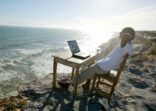 Man relaxing by seashore with computer