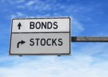 Road sign with words bonds and stocks. White two street signs with arrow on metal pole on blue sky background.