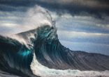 Tall powerful cross ocean wave breaking during a dark, stormy evening.